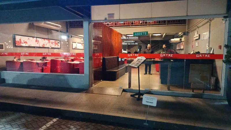 Entrada do restaurante à noite, com o salão iluminado e bancos vermelhos